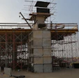 An inşaat halinde bridge with scaffolding and concrete pillars, situated in an open area with clear skies. A crane and various inşaat malzemeleri are visible, with a vehicle parked nearby.